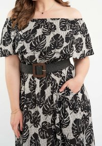 Mustavalkoinen olkaimeton mekko, jossa on lehtikuosi, teksturoitua kangasta, vyötärölle kiristetty paksulla mustalla vyöllä, jossa on neliömäinen metallipitsi.