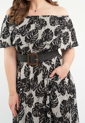 Robe noire et blanche à bretelles dénudées avec motif de feuilles, en tissu texturé, cintrée par une large ceinture noire avec une boucle en métal carrée.