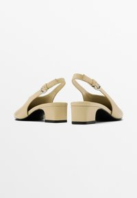 Décolleté beige con cinturino dietro, punta tonda, tacco basso a blocco e dettaglio con fibbia sul cinturino, caratterizzati da una superficie in pelle liscia e un design minimalista.