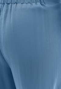 Blauwe stoffen broek met een gladde textuur en een elastische tailleband, met een zachte val en stikdetails langs de naden.