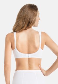 Senza ferretto bianco con spalline larghe, tessuto liscio, schiena arrotondata e chiusura a gancio. Presenta un design semplice e senza cuciture con una texture morbida.