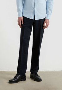 Ciemnoniebieskie spodnie materiałowe o dopasowanym kroju, wykonane z gładkiej tkaniny. W zestawie z czarnymi butami na sznurówki. Minimalistyczny design, bez widocznych wzorów.