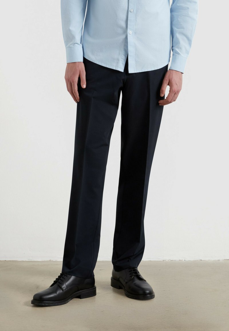 Ciemnoniebieskie spodnie materiałowe o dopasowanym kroju, wykonane z gładkiej tkaniny. W zestawie z czarnymi butami na sznurówki. Minimalistyczny design, bez widocznych wzorów.