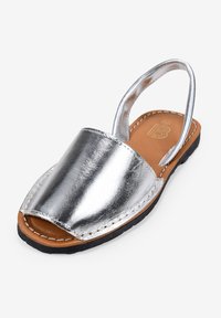 Sandalia de piel plateada con diseño de punta descubierta, talón abierto y suela de goma negra. Presenta detalles de costura y un acabado metálico suave.