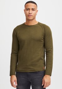 Donkergroene langemouwen shirt met een gestructureerde afwerking, ronde hals en raglanmouwen. Kleine gemerkte patch nabij de zoom.
