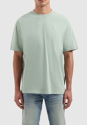 Light green cotton t-shirt with a crew neck, short sleeves, and a small embroidered logo on the chest, paired with light blue jeans.