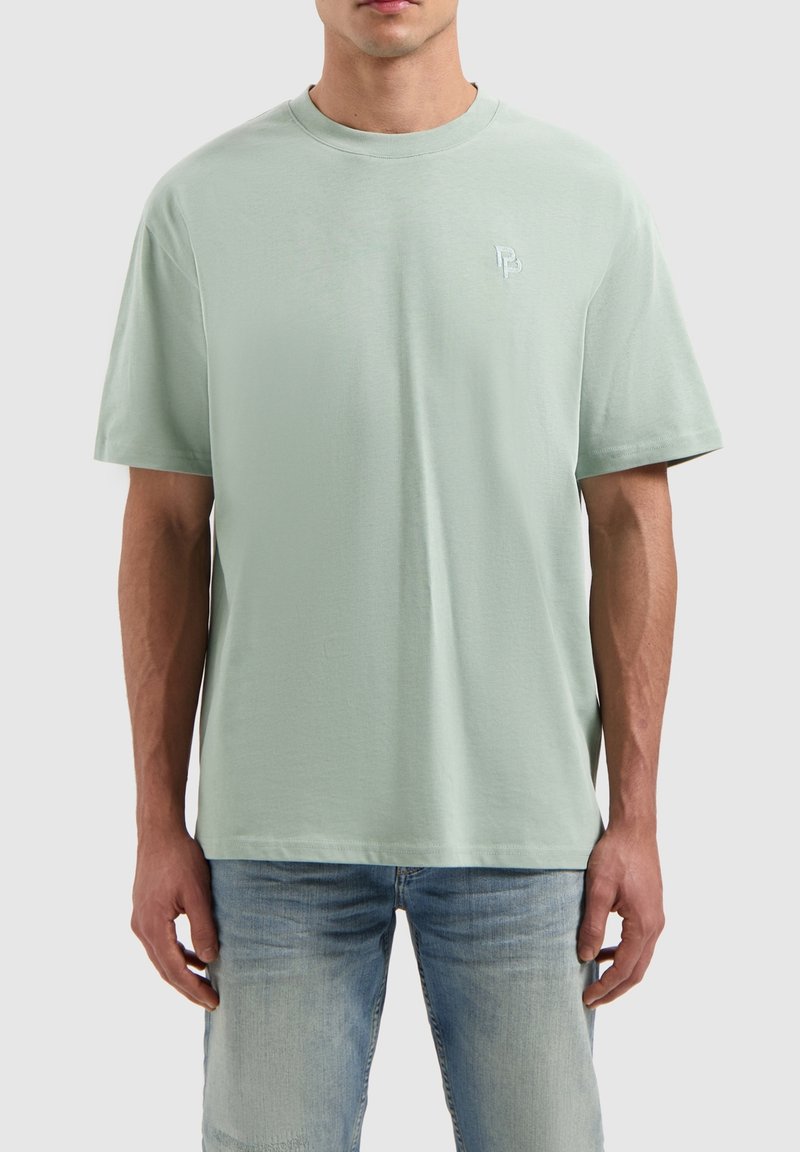 Lichtgroene katoenen t-shirt met een ronde hals, korte mouwen en een klein geborduurd logo op de borst, gecombineerd met lichtblauwe jeans.