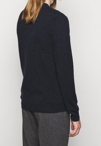 Mörkblå stickad tröja med långa ärmar, åtsittande mudd och rund halsringning. Slät textur med enkel design utan synliga mönster.