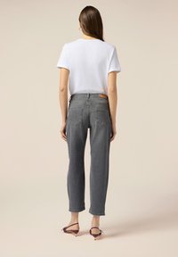 Jeans alti grigi con un fit rilassato e tasche posteriori visibili, abbinati a una t-shirt bianca semplice e sandali viola con cinturini.