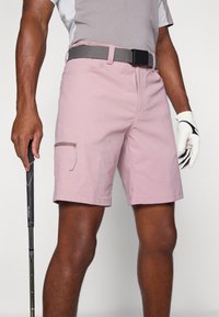 Pale pink golf shorts made of lightweight fabric, featuring a side zipper pocket, flat front, and a grey belt with a black buckle.