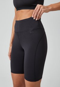 Zwarte sportshorts met een hoge tailleband, gemaakt van soepel, rekbaar materiaal. Voorzien van een logo en naden, ontworpen voor comfort en beweging.
