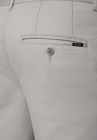 Szare, teksturowane spodnie mają tylną kieszeń z guzikiem oraz małą czarną metkę z napisem "PRÓHNIK". Tkanina ma subtelny wzór splotu.