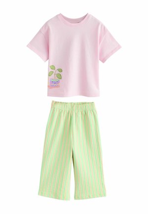 Rosa Kurzarmshirt mit einer Grafik einer lächelnden Topfpflanze, kombiniert mit grünen und pfirsichfarbenen, vertikal gestreiften, weit geschnittenen Hosen.