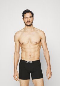 Svarte Levi's boxershorts med hvit logobånd, tilpasset design, glatt tekstur, modellen står mot en enkel lys bakgrunn.