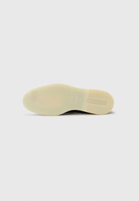 Svart lädersula med en slät yta, något genomskinlig beige gummi och en logotyp tryckt nära hälen. Platt, rundad form.
