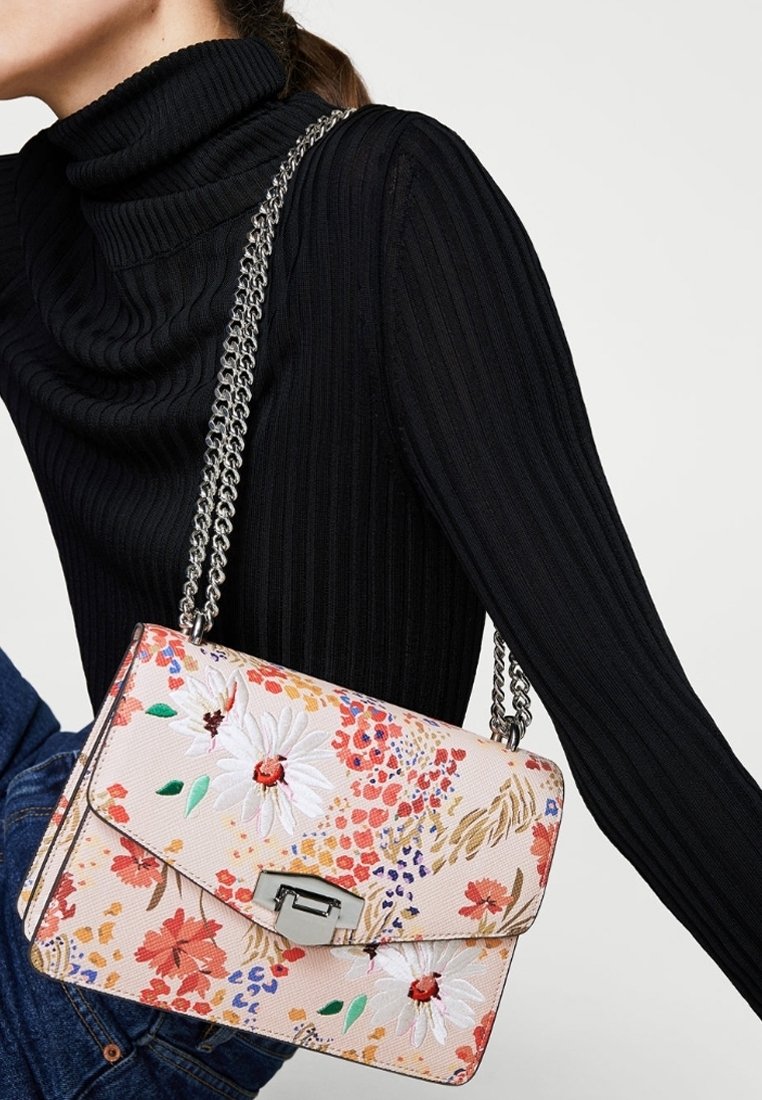 Blumen-Crossbody-Tasche aus pinkem Stoff mit bestickten weißen Gänseblümchen und bunten Akzenten. Verfügt über einen silbernen Kettenriemen und einen Metallverschluss.