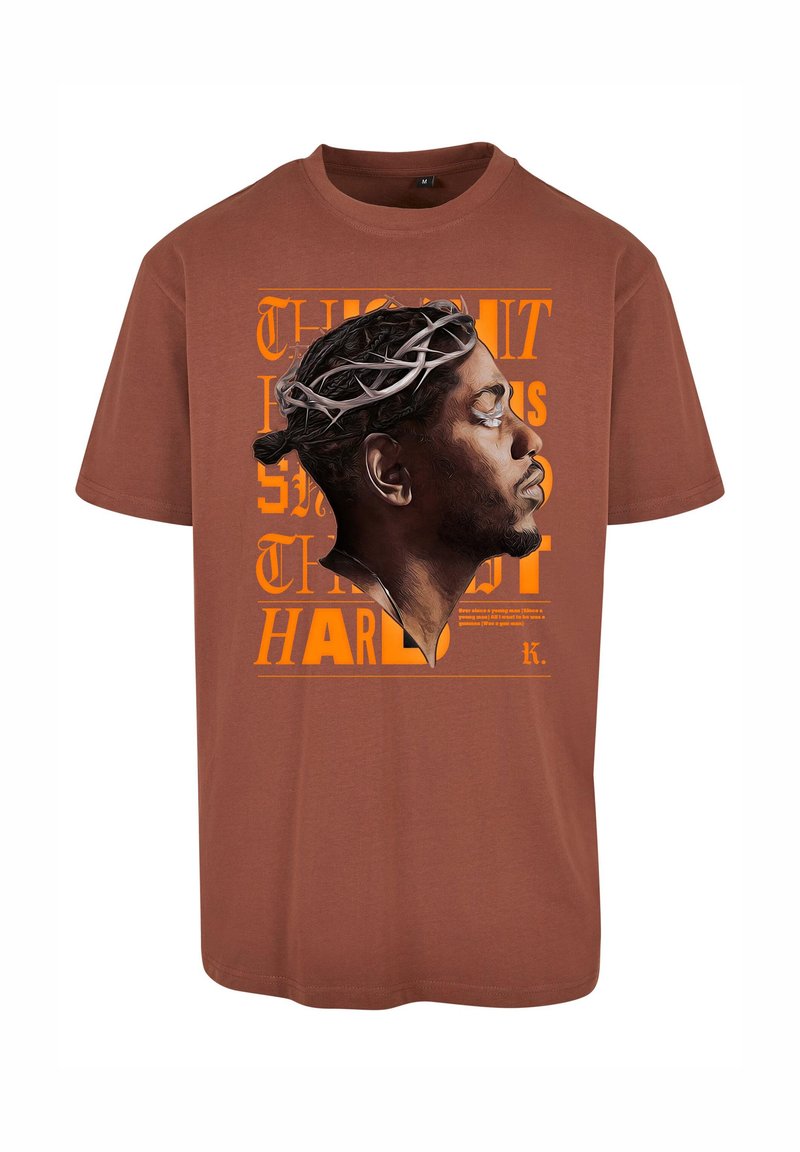 Brun bomulds t-shirt med et grafik af en profil med en tornkrone, fremhævet af orange tekst, der læser "SANDHEDEN GØR ONDT."