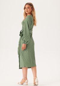 Groene textuur midi-jurk met lange mouwen, een gestrikt middel en een losse pasvorm. Gekleed met witte blokhak sandalen. Eenvoudig en elegant.