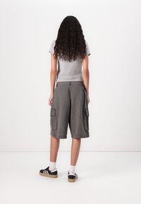 Pilkos krovinių šortai su dviem šoninėmis kišenėmis ir laisvu siluetu. Sujungti su pilku marškinėlių ir juodais batais ant balto fono.