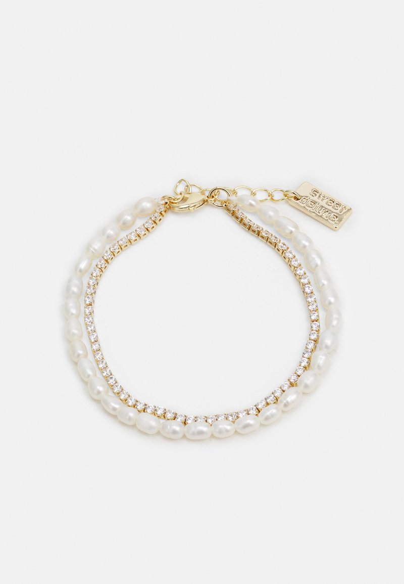 Dubbelslingad armband med vita pärlor och guldaccenter, kombinerat med en rad klara rhinestones för extra glans.