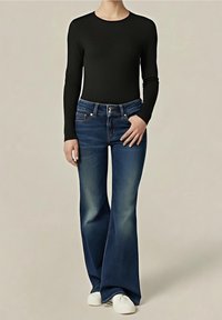 Personne portant un jean évasé bleu foncé, un haut noir moulant à manches longues et des chaussures blanches sur un fond clair uni.
