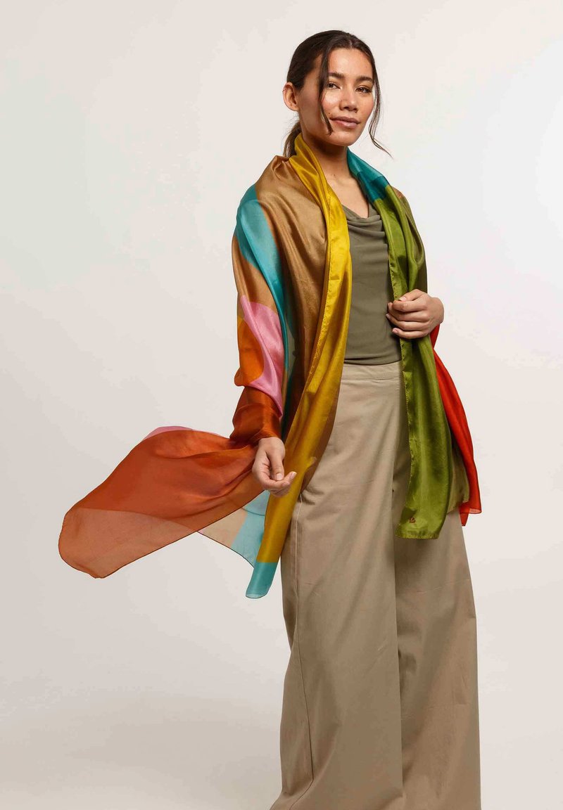 Foulard trasparente multicolore con una sfumatura di arancione, blu, verde e rosa, che cade elegantemente su una parte superiore unita e pantaloni color crema.
