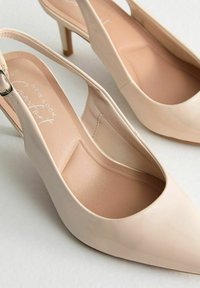 Décolleté color beige in vernice con punta affilata, lieve plateau e tacco a stiletto piccolo. L'interno presenta una texture morbida.