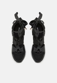 Black sandals with a mesh toe box, lace-up design, and satin ribbon accents. Features a textured surface and flexible material for comfort.