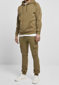 Olivově zelená mikina s kapucí na stažení a přední kapsou, doplněná o odpovídající cargo kalhoty s bočními kapsami a žebrovanými manžetami.