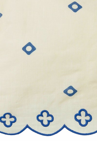 Nappe blanche ornée de motifs en diamant et circulaires brodés en bleu, avec un bord festonné et une finition en coton texturé.