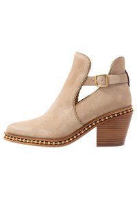 Beżowe zamszowe botki sięgające kostki z wycięciami po bokach, ozdobione złotymi ćwiekami, złotym paskiem z klamrą oraz na słupkowym drewnianym obcasie.