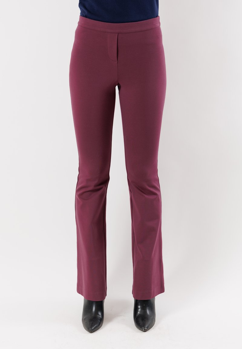 Pantaloni slim-fit bordeaux con texture liscia, orlo svasato e vita. Abbinati a stivali neri con punta a forbice e tacco alto.