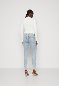 Jeans de mezclilla de color azul claro con un diseño ajustado, que presentan un sutil patrón texturizado y bolsillos traseros, combinados con una blusa blanca de canalé.