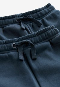 Marina blå mjukisbyxor med elastisk midja, snörning och två fickor, tillverkade av mjukt bomullsmaterial med ribbade detaljer.