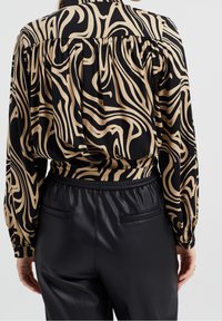 Blus med svart och beige abstrakt virvelmönster, med en rynkad bakdesign, långa ärmar och en avslappnad passform parat med svarta läderbyxor.