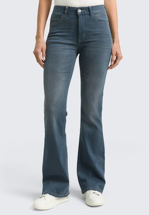 Blaue Jeans mit Glockenschnitt und mittelhoher Taille, vorderen Taschen und leichter Ausbleichung. Tragen Sie sie mit weißen Sneakers für einen lässigen Look.