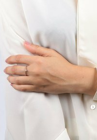 Silberring mit einem kleinen Edelsteinelement, auf einer Hand platziert, die gegen einen hellen Stoff lehnt. Die Hand hat ein natürliches Finish mit kurzen, polierten Nägeln.