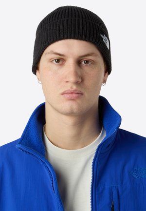Black ribbed beanie and blue zip-up jacket made of soft material. The jacket's collar is up, revealing a light-colored shirt underneath.