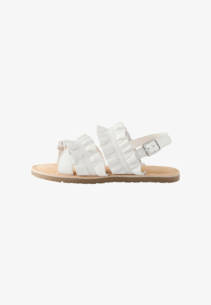 White flat sandal with ruffled straps, adjustable ankle buckle, and beige textured sole shown from the side on a white background.