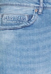 Lichtblauwe denim jeans met een gestructureerde afwerking, voorzien van een label dat op de achterzak is gestikt met de tekst "CARS JEANS."
