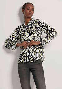 Langdurige blouse in zwart, wit en geel abstract patroon; voorzien van een knoopkraag en elastische manchetten. Gecombineerd met donkere denim.