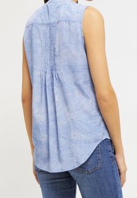 Maglietta blu senza maniche con un delicato motivo a onde, dettaglio plissettato sulla schiena e orlo curvo, abbinata a jeans in denim.