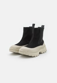 Botas de tobillo gruesas en negro y crema con una suela de goma lisa, paneles laterales elásticos y lengüetas traseras para facilitar su colocación. Diseño de parte superior texturizada.