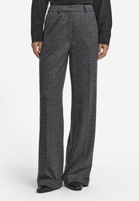 Grå herringbone byxor med vida ben och uppvikta fållar, bärs tillsammans med svarta spetsiga skor och en svart långärmad skjorta.