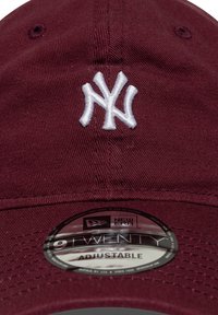 Burgundy baseball cap made of cotton, featuring a white embroidered "NY" logo. Adjustable strap with a circular New Era tag on the inside.
