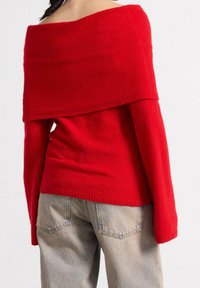 Rød off-shoulder sweater med en blød tekstur og lange ærmer, båret over et lyst blått, løst passende par jeans.