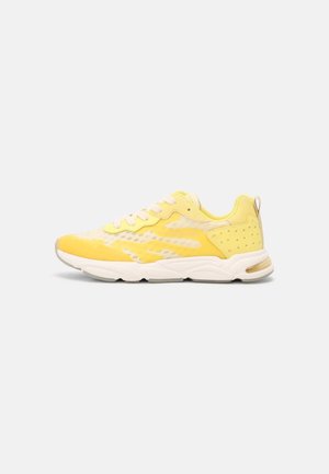 Baskets de sport jaunes et beige avec semelle blanche, empeigne en mesh, design à lacets et détail à motif étoilé au talon sur fond gris clair.