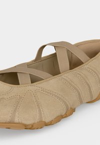 Beige suède platte schoen met gekruiste elastische banden en een gestructureerde rubberen zool voor casual gebruik.