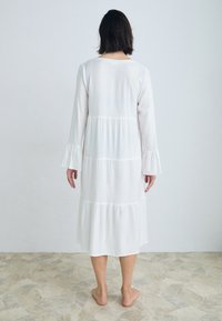 Vestido branco de manga longa com design em camadas e punhos franzidos. Tecido suave, até ao joelho, com um corte descontraído e estilo minimalista.
