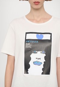 Weißes T-Shirt mit einem grafischen Druck eines Gesichts mit blauen Akzenten, schwarzen Konturen und Text. Rundhalsausschnitt und weiche Textur.